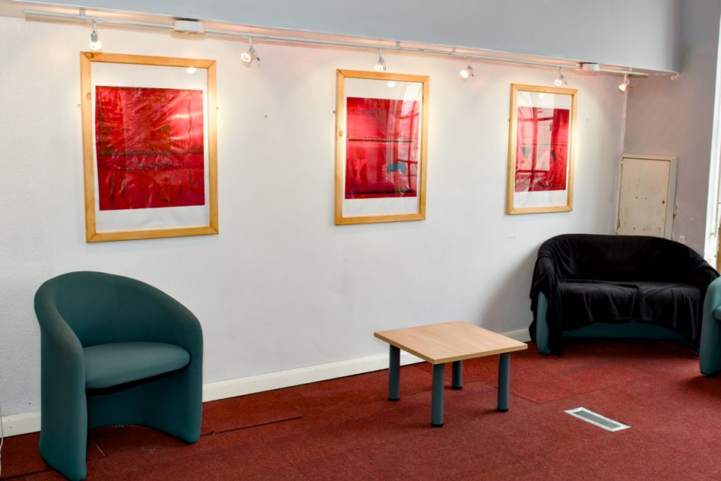 an exhibition wall displaying three red abstract paintings